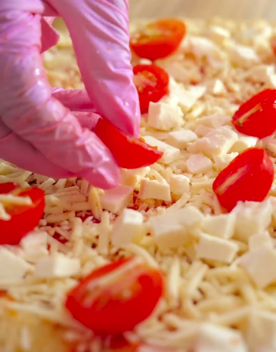 A gloved hand scattering cherry tomatoes over mozzarella on a Crozza